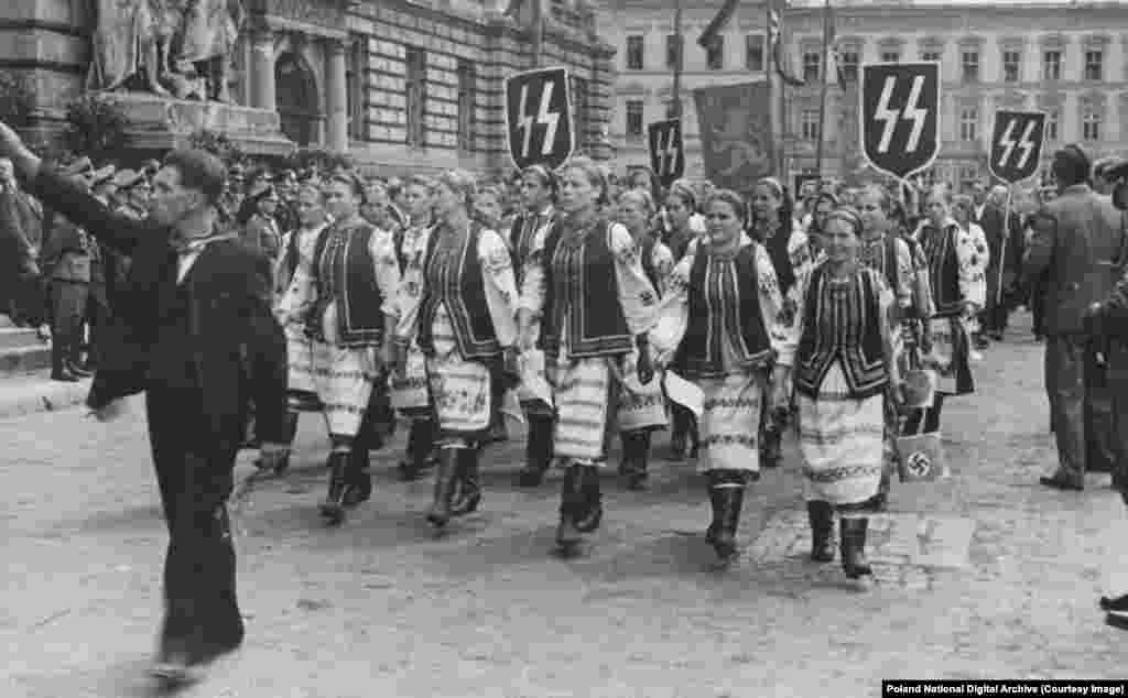 Ukrajinke u tradicionalnoj nošnji paradiraju pod nacističkim zastavama u Lavovu tokom službene posjete Hansa Franka, njemačkog poglavara Poljske pod nacističkom okupacijom. Mnogi ukrajinski nacionalisti su prema nacističkoj invaziji zauzeli stav &quot;neprijatelj mog neprijatelja je moj prijatelj&quot;, pripisujući Nijemcima zasluge za istjerivanje komunističkih boljševika. Neki Ukrajinci su aktivno učestvovali u masovnim ubistvima Jevreja, dok su drugi, &quot;pojedinci, a ponekad i cijela sela&quot;, rizikovali sve kako bi zaštitili Jevreje od nacista.