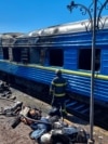 Пожежники стоять перед вагоном пасажирського потяга, пошкодженого внаслідок російського удару по Херсону, 3 травня 2023 року