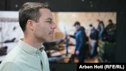 Američki fotoreporter Brendan Hofman na izložbi "Ukrajina: ratni zločin", dok se u pozadini vidi fotografija koju je napravio drugog dana invazije.