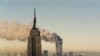 Turnurile gemene de la World Trade Center arzînd în spatele blocului Empire State Building, New York, 11 septembrie 2001.