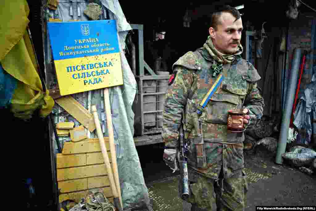 Український військовий із 93-ї окремої механізованої бригади відпочиває за кавою та сигаретою. Знак, який військові зняли з Пісківської сільської ради, висить на «Позиції 18»