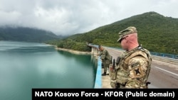 Një ushtar i KFOR-it dhe pjesëtarë të FSK-së qëndrojnë mbi njërën nga urat në Liqenin e Ujmanit, ku më 29 korrik 2025 po zhvillohen kërkime.