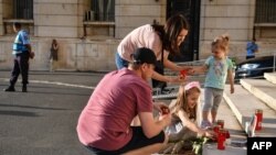 Dramele nu se uită. O familie aprinde lumânări pe scările Ministerului de Interne, iar lângă se află portretul Alexandrei, fata de 15 ani care a fost omorâtă după ce a sunat de trei ori la 112 să anunțe că a fost răpită. Imagine din 27 iulie 2019. 