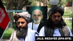 Taliban members stand in front of a portrait of Afghan President Ashraf Ghani as they attend a ceremony at the governor's office after being released, in Herat on May 26.