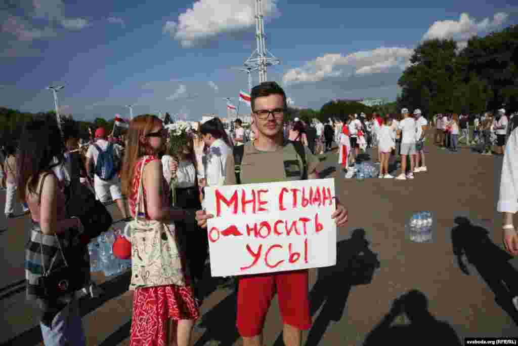 Čovjek drži znak na kojem piše "stid me je da nosim brkove", referirajući se na činjenicu da Lukašenka nosi brkove. 
