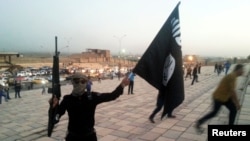 Borac "Islamske države Iraka i Levanta" (ISIL) drži zastavu ISIL-a i oružje na ulici u gradu Mosulu 23. juna 2014. 