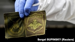 Украинский криминалист показывает нашивки, найденные на теле российского солдата, 11 мая 2022 года